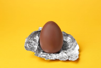 Tasty chocolate egg with foil on orange background