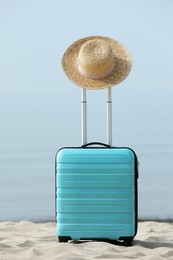 Photo of Turquoise suitcase with straw hat on sandy beach