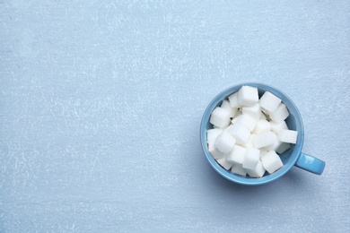 Photo of Cup with refined sugar cubes on grey background, top view