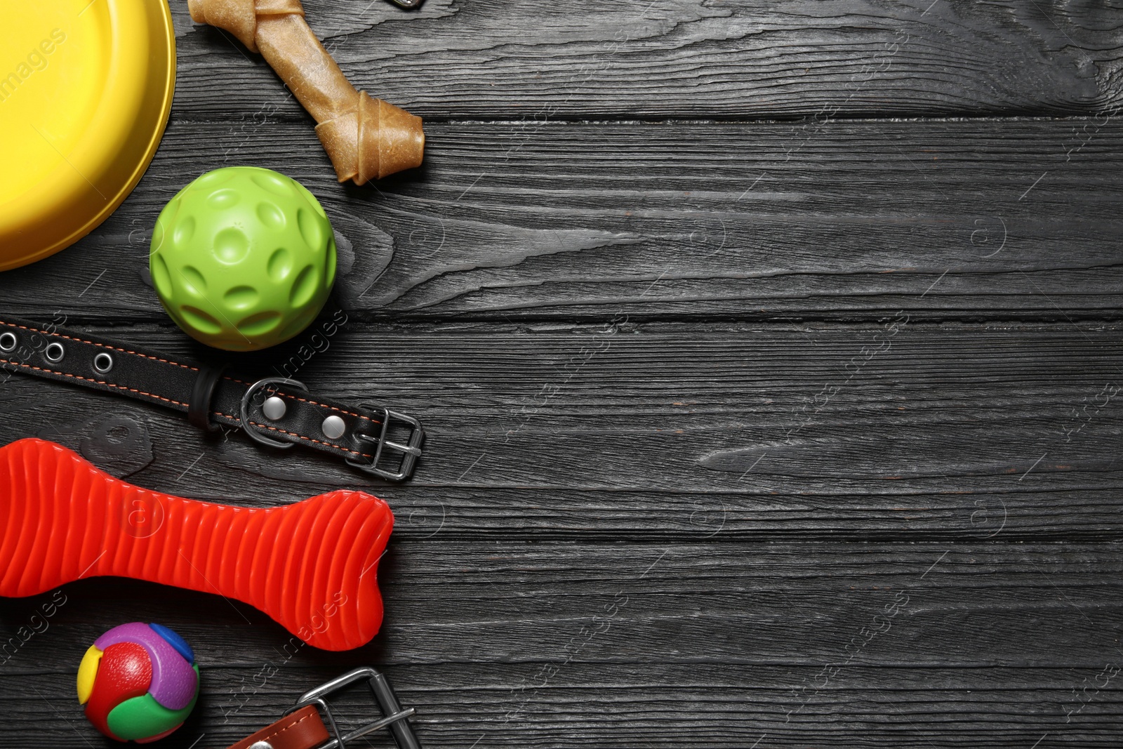 Photo of Flat lay composition with dog collar and toys on black wooden table. Space for text