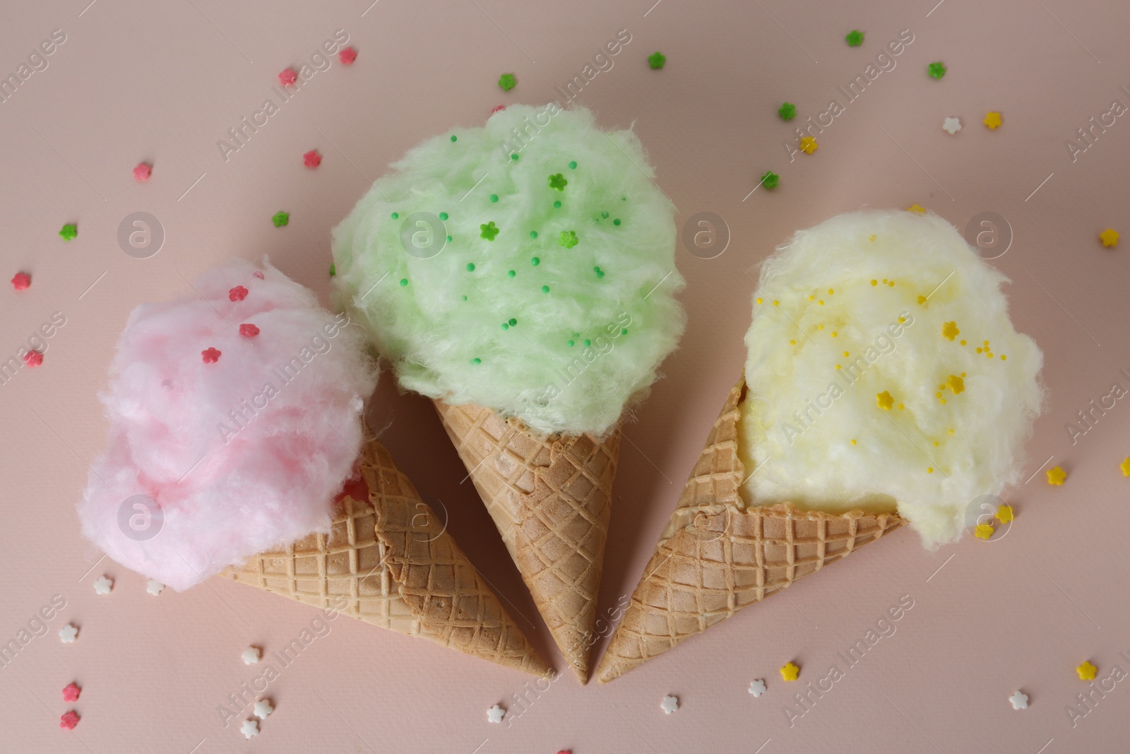 Photo of Sweet cotton candies in waffle cones on beige background, flat lay