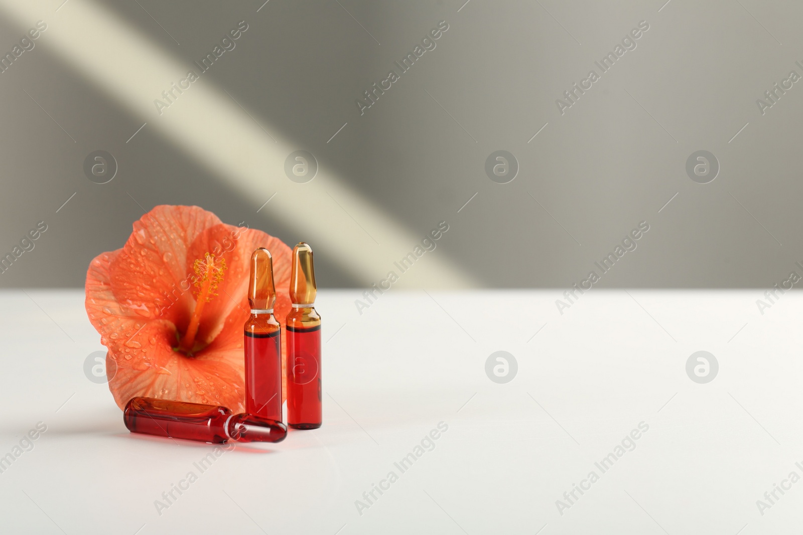 Photo of Skincare ampoules and hibiscus flower on white table. Space for text