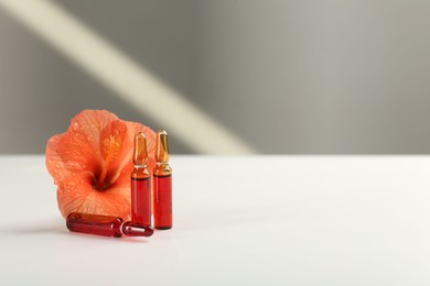 Skincare ampoules and hibiscus flower on white table. Space for text