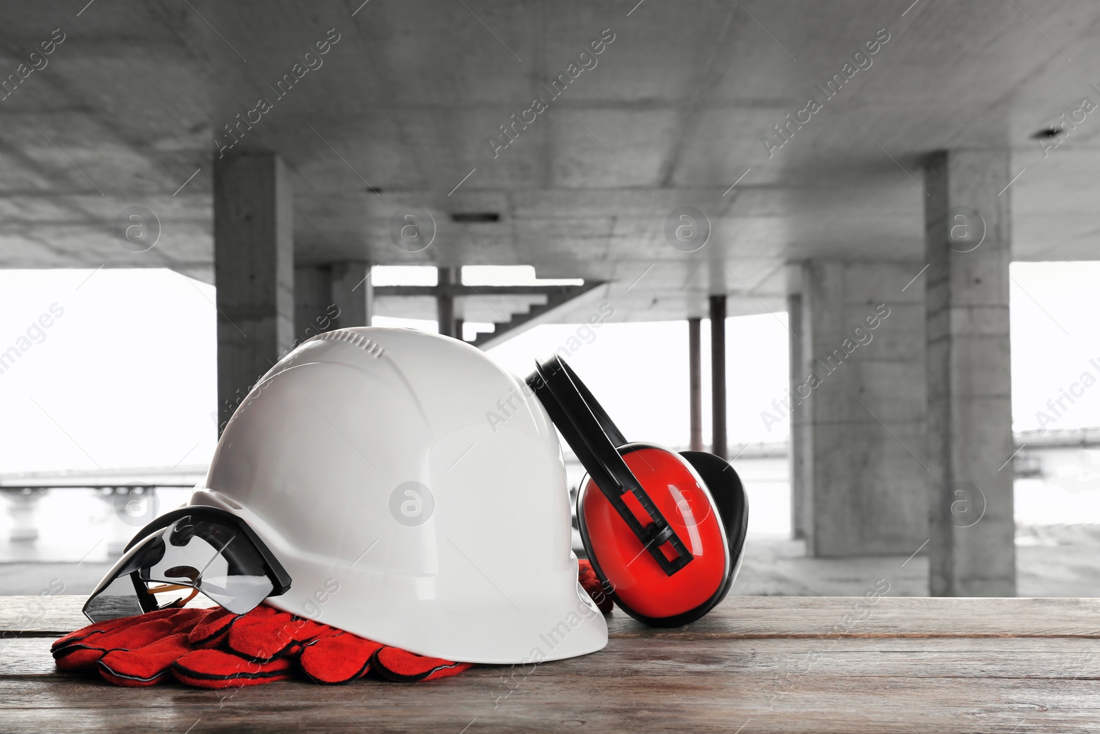 Image of Safety equipment. Hard hat, goggles, gloves and protective headphones on wooden surface inside of unfinished building, space for text