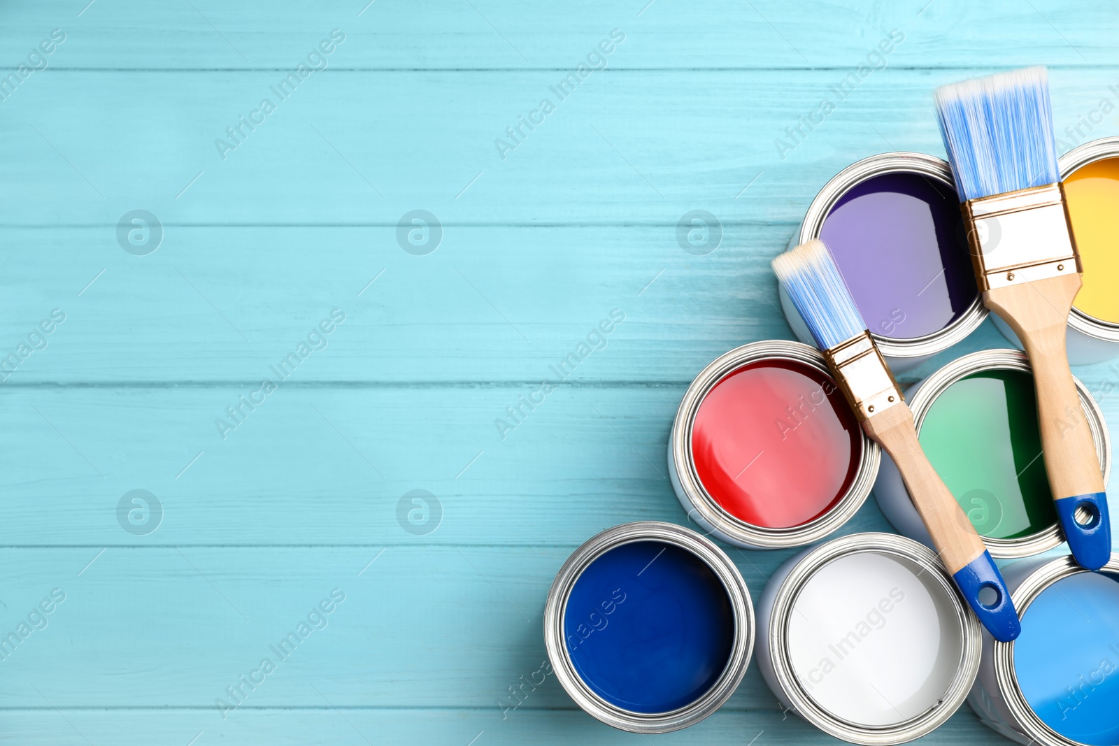 Photo of Open cans with paint and brushes on blue wooden table, flat lay. Space for text