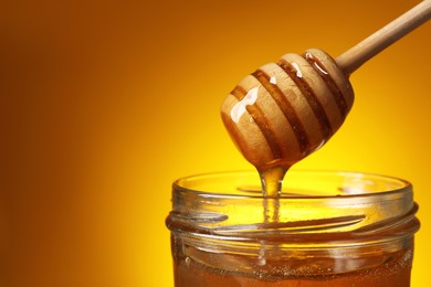 Photo of Pouring honey from dipper into jar against golden background, closeup. Space for text