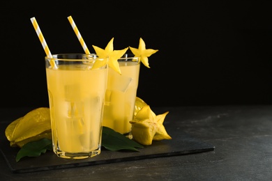 Photo of Delicious carambola juice in glasses on black table. Space for text