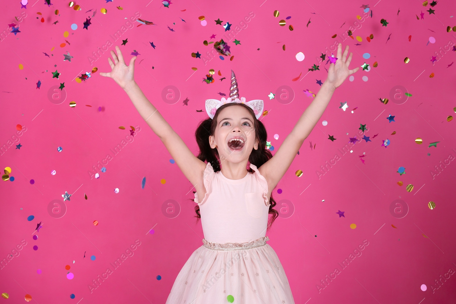 Photo of Adorable little girl and falling confetti on pink background