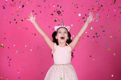Adorable little girl and falling confetti on pink background