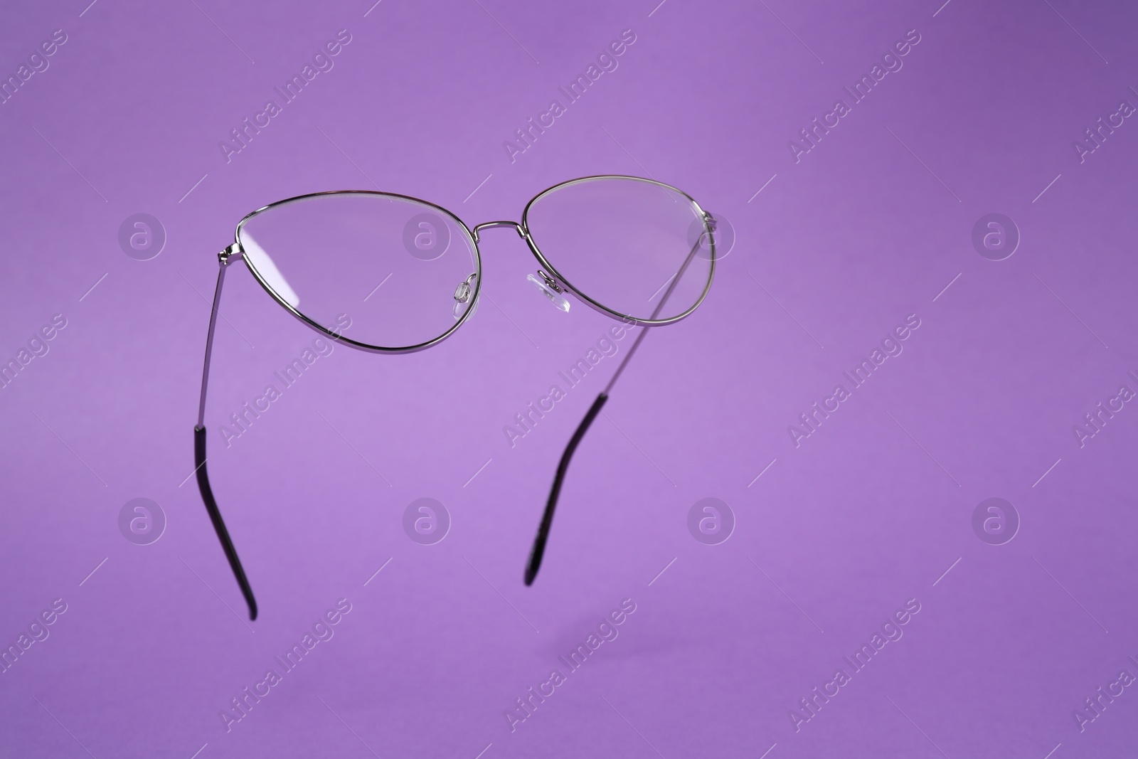 Photo of Stylish pair of glasses with metal frame on purple background. Space for text