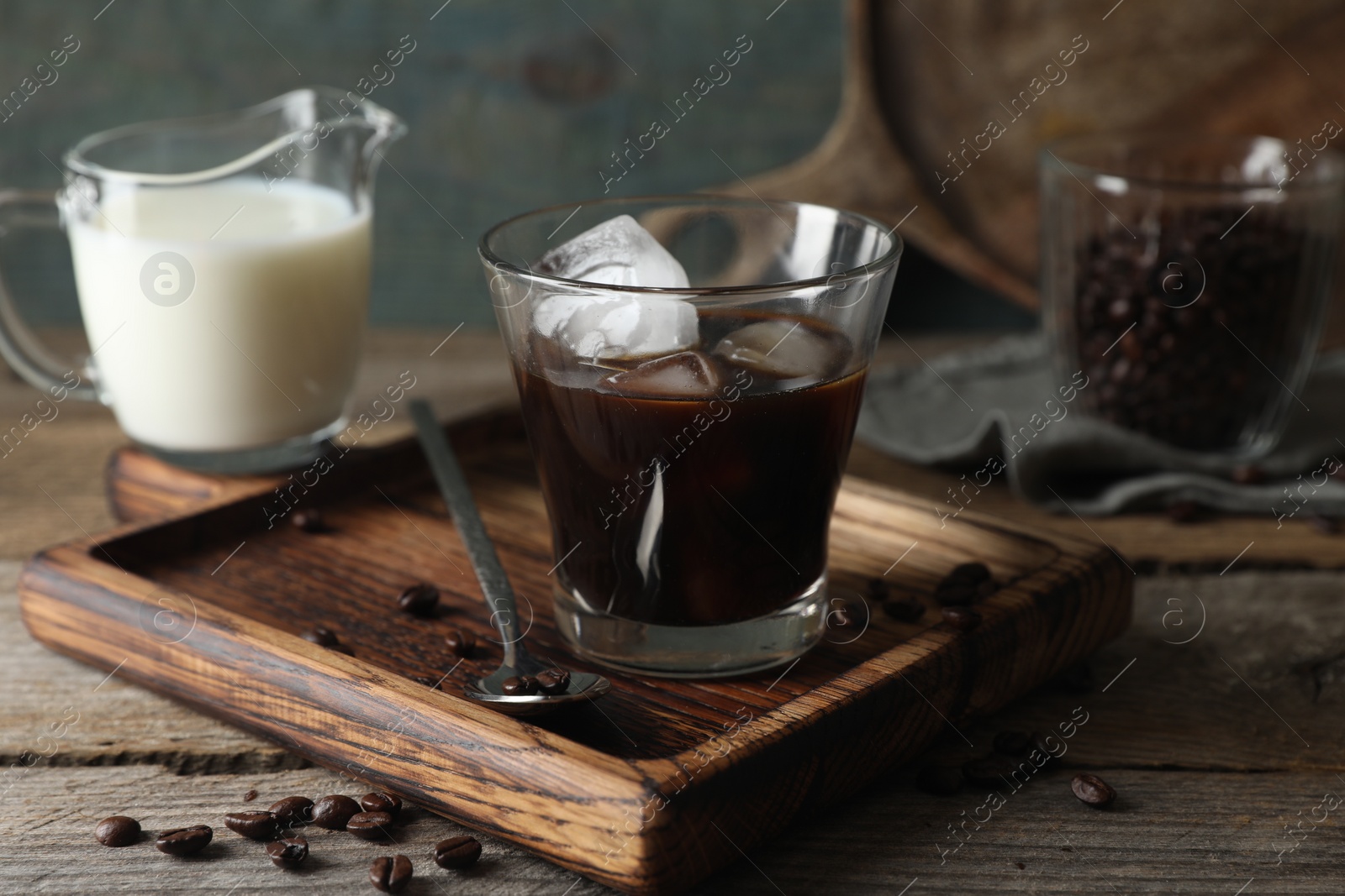 Photo of Glass of delicious iced coffee, milk and beans on wooden table