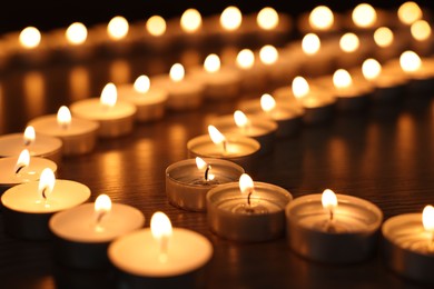 Burning candles on wooden table in darkness, closeup