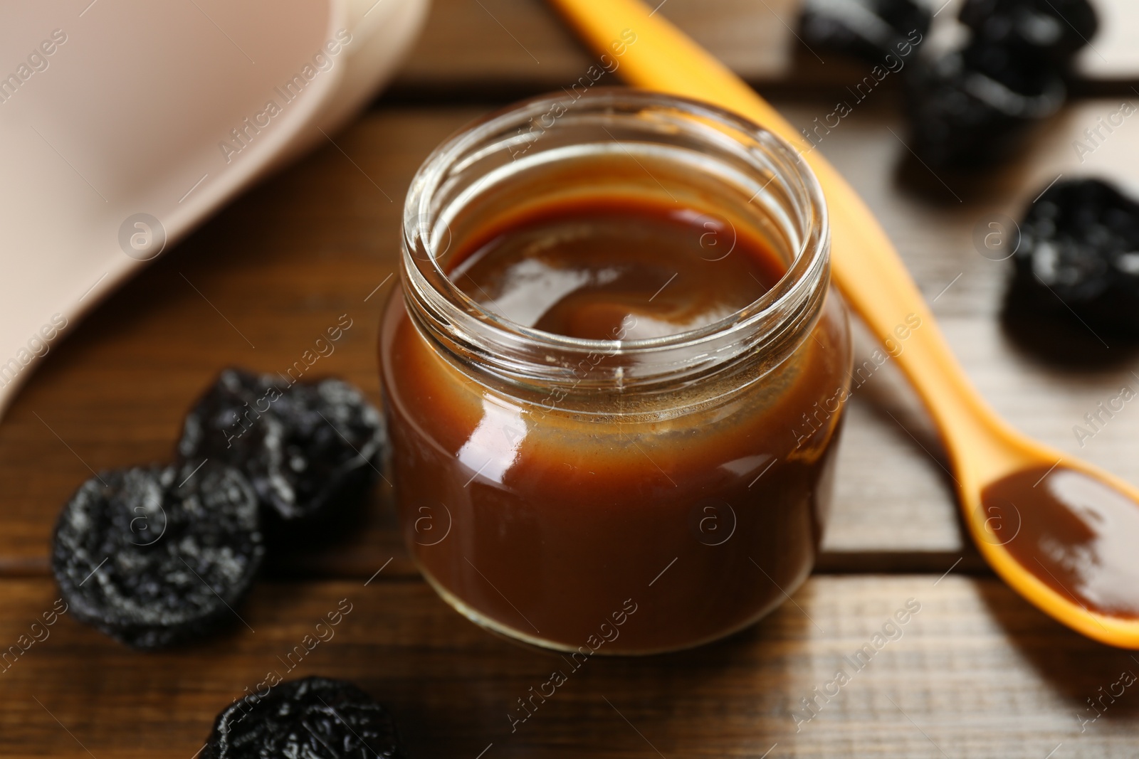 Photo of Tasty baby food in jar, spoon and dried prunes on wooden table, closeup