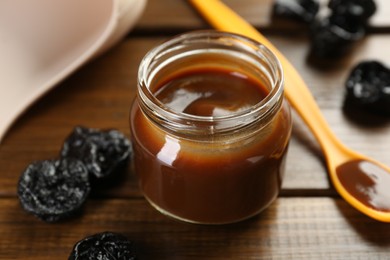 Photo of Tasty baby food in jar, spoon and dried prunes on wooden table, closeup