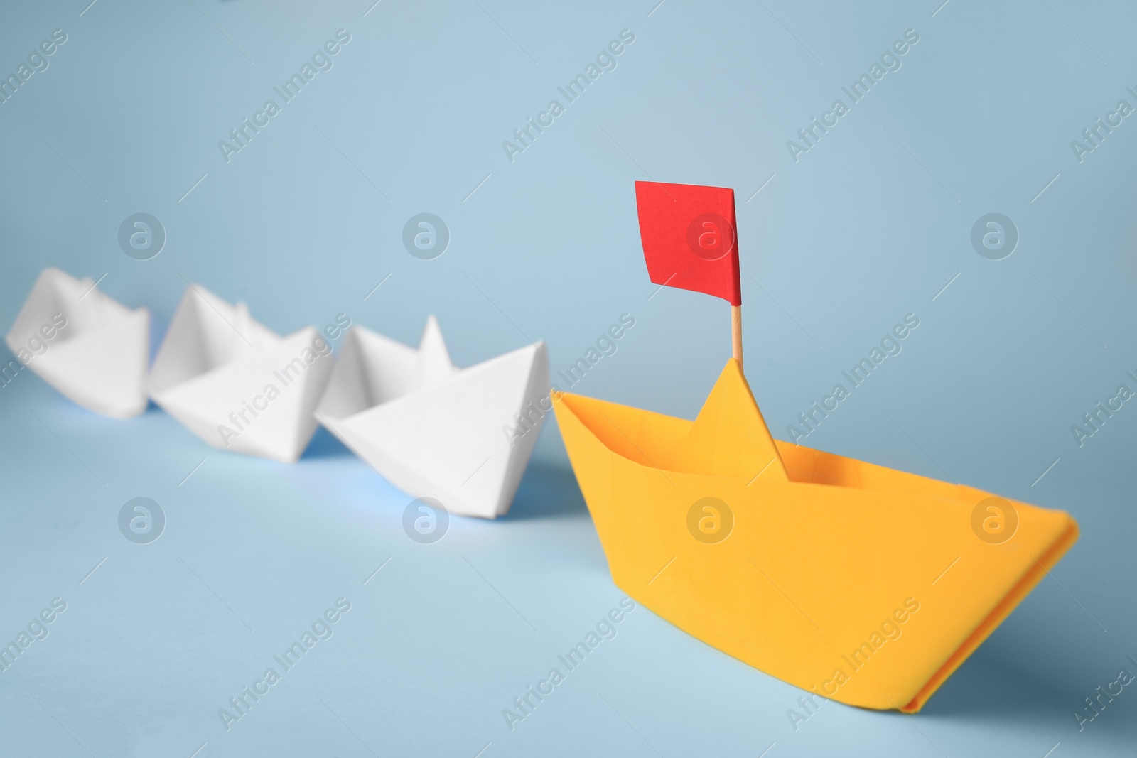 Photo of Group of paper boats following yellow one on light blue background. Leadership concept