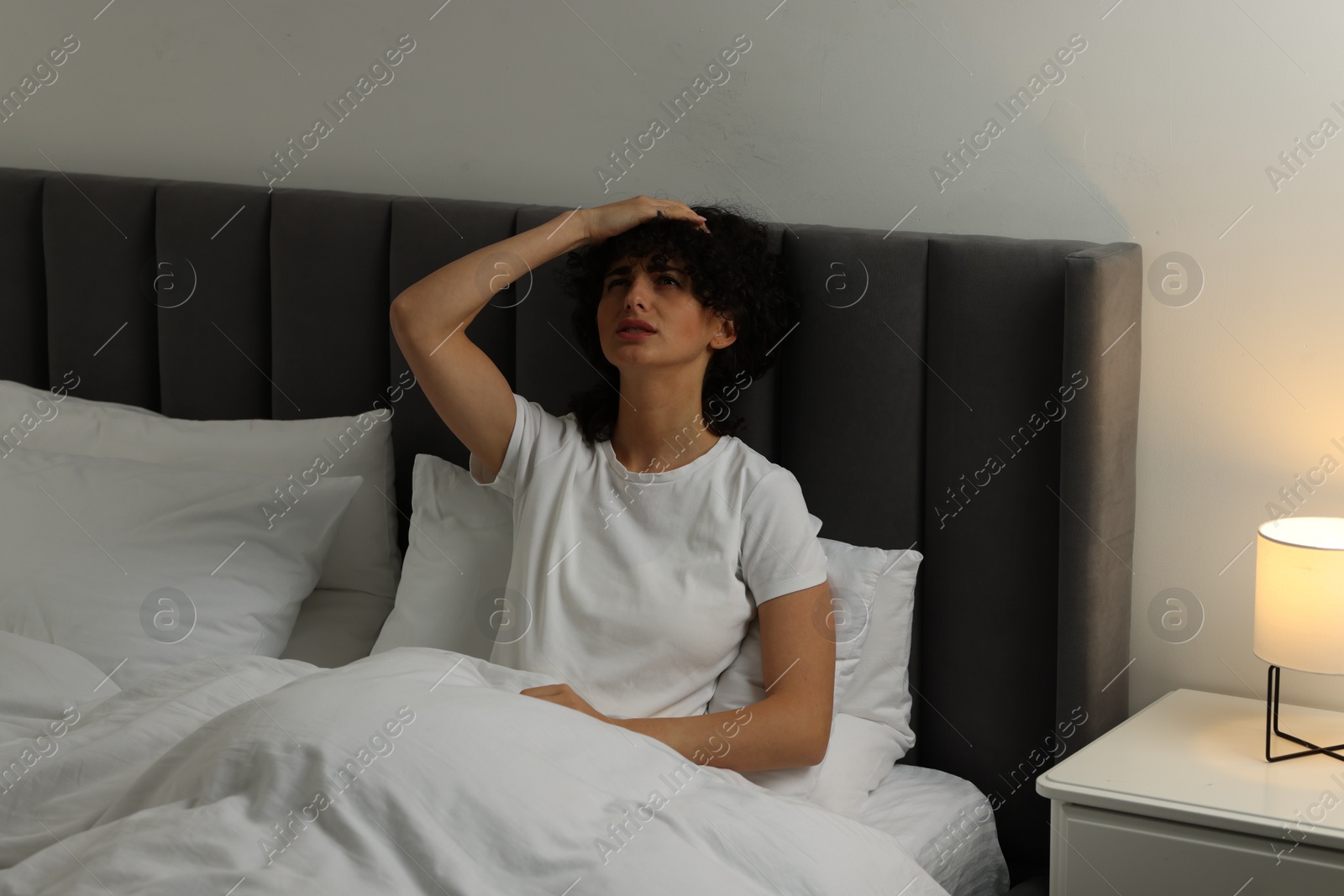 Photo of Young woman suffering from headache in bed at night