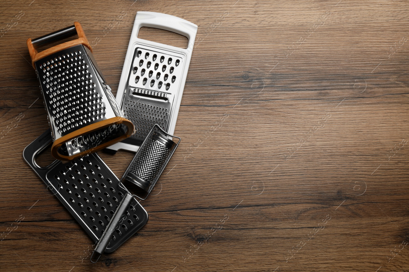 Photo of Different modern graters on wooden table, flat lay. Space for text