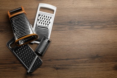 Photo of Different modern graters on wooden table, flat lay. Space for text