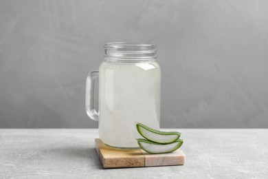 Photo of Tasty aloe juice in mason jar and cut fresh leaves on light grey table