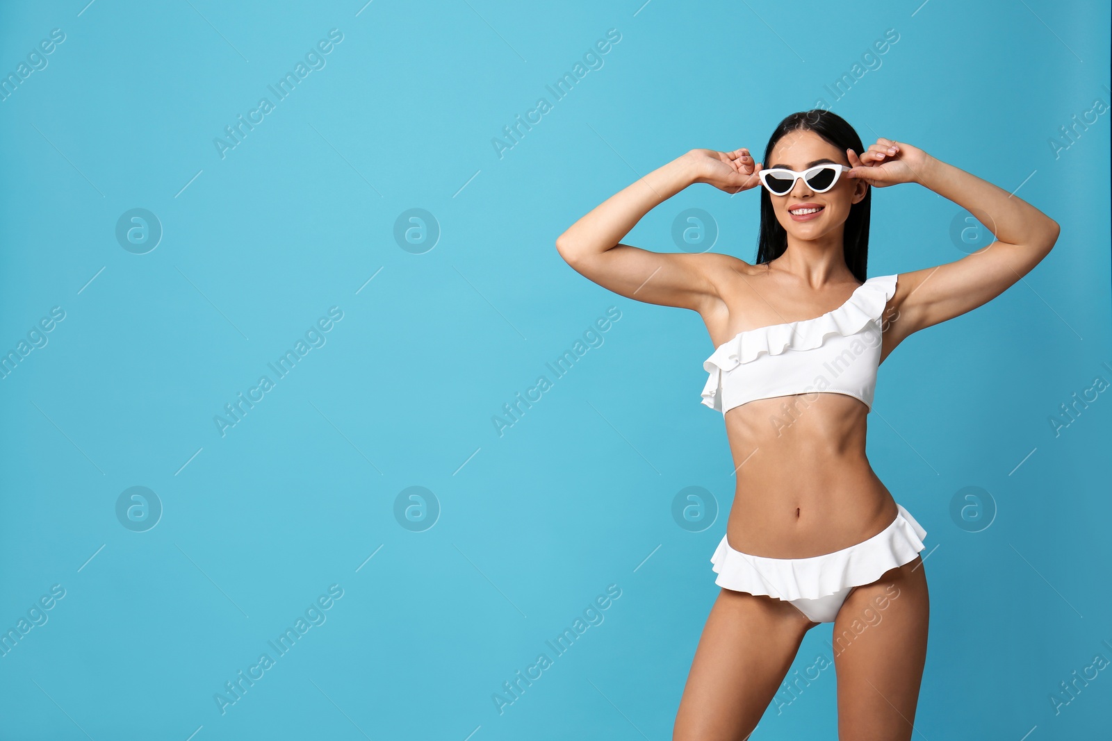 Photo of Beautiful young woman in white bikini with sunglasses on light blue background. Space for text