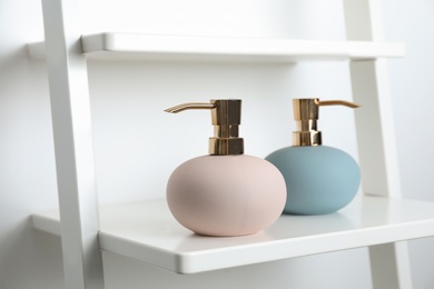 Photo of Stylish soap dispensers on shelf near light wall