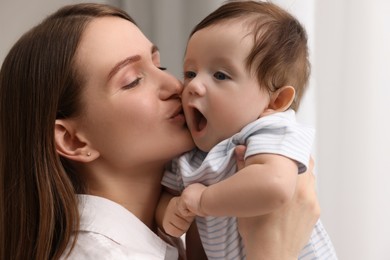Photo of Happy mother kissing her little baby indoors, closeup