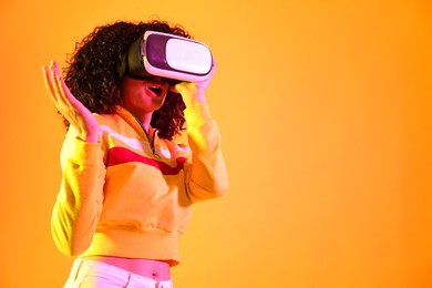 Photo of Beautiful young woman with virtual reality headset on color background in neon lights. Space for text