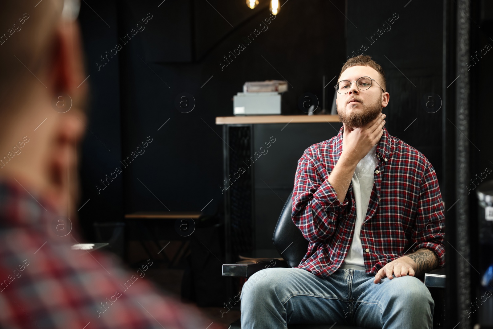 Photo of Young bearded man near mirror in barbershop