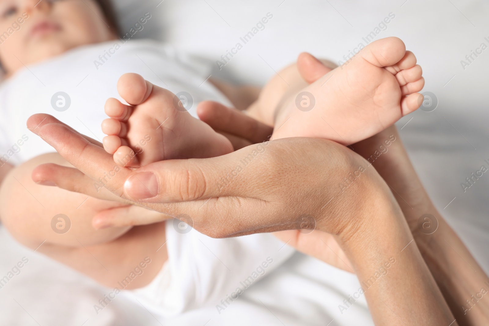 Photo of Mother holding legs of her little baby on bed, closeup