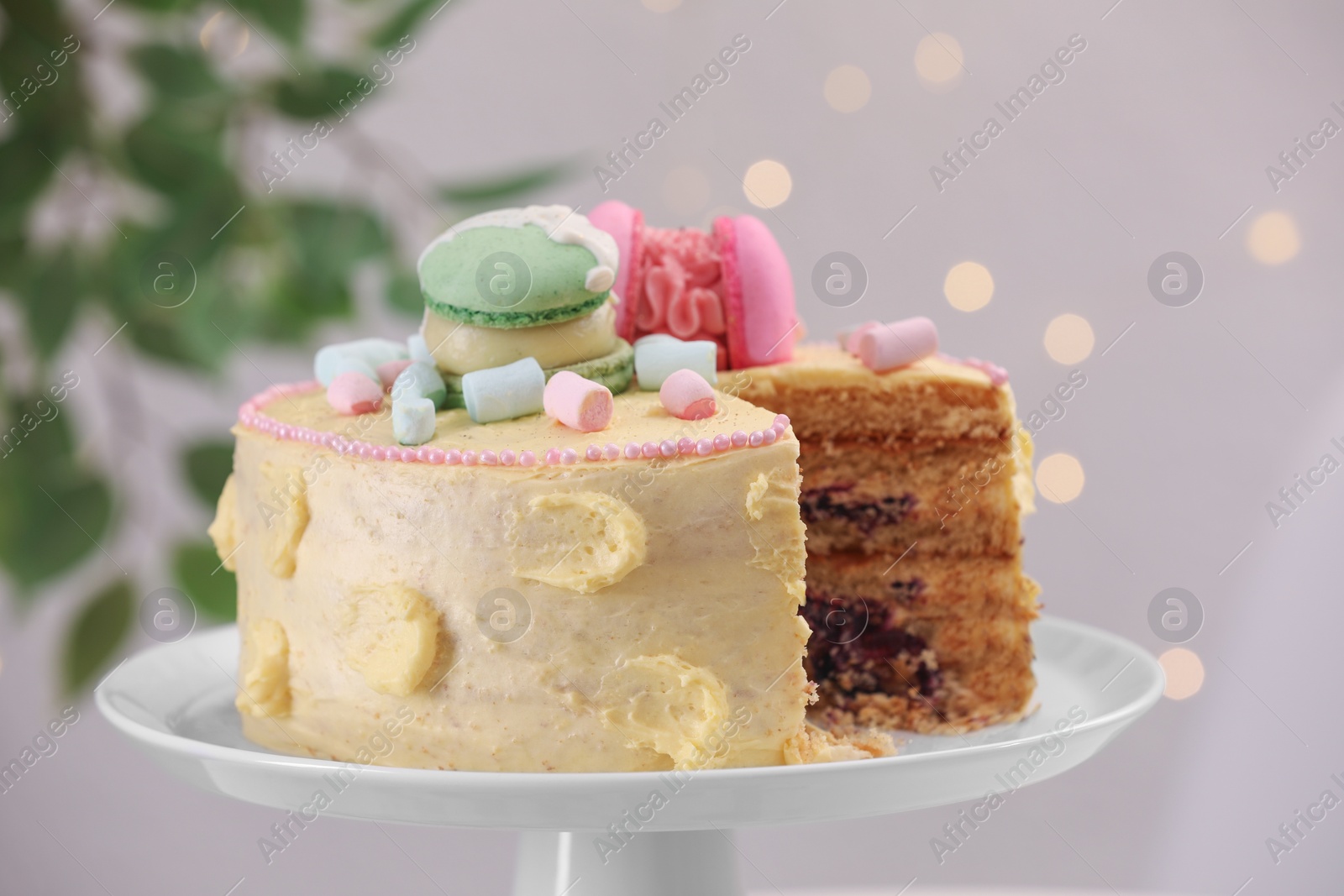 Photo of Delicious cake decorated with macarons and marshmallows against blurred lights, closeup