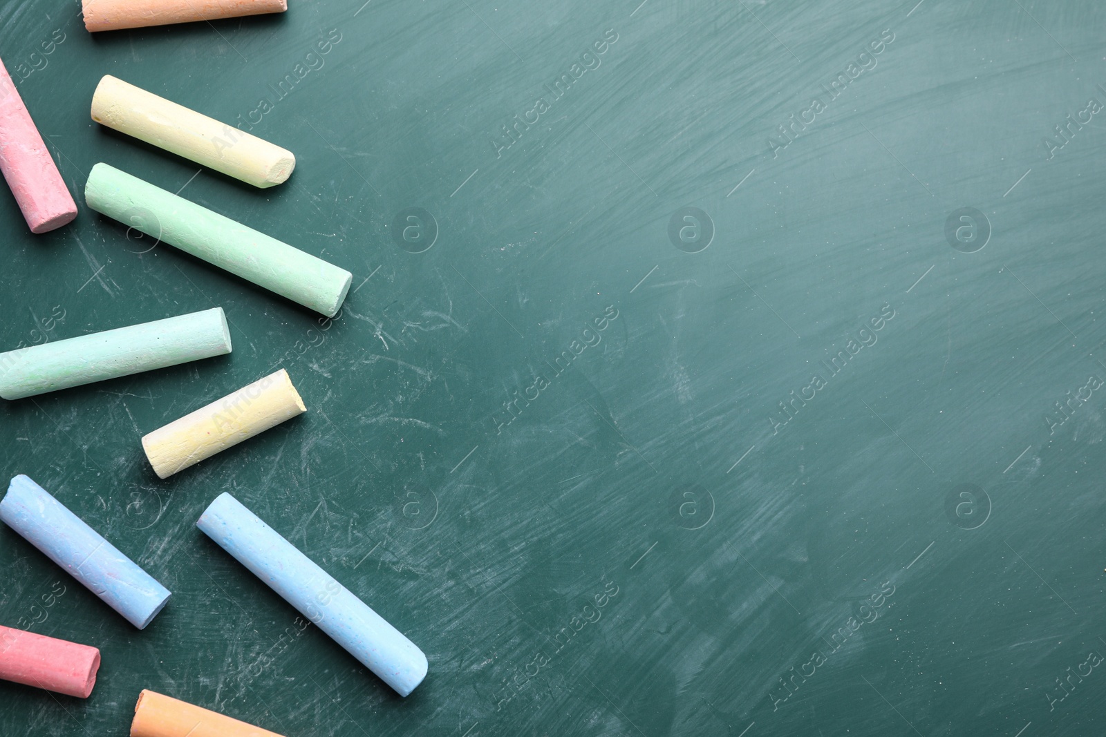 Photo of Pieces of color chalk on greenboard, flat lay. Space for text