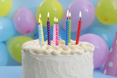 Delicious cake with burning candles and festive decor on light blue background, closeup