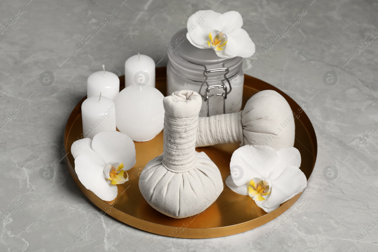 Photo of Tray with herbal bags, candles, scrub and beautiful flowers on grey marble table. Spa products