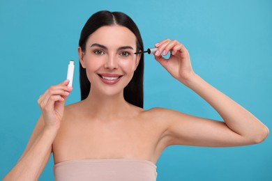 Beautiful woman applying serum onto her eyelashes on light blue background. Cosmetic product