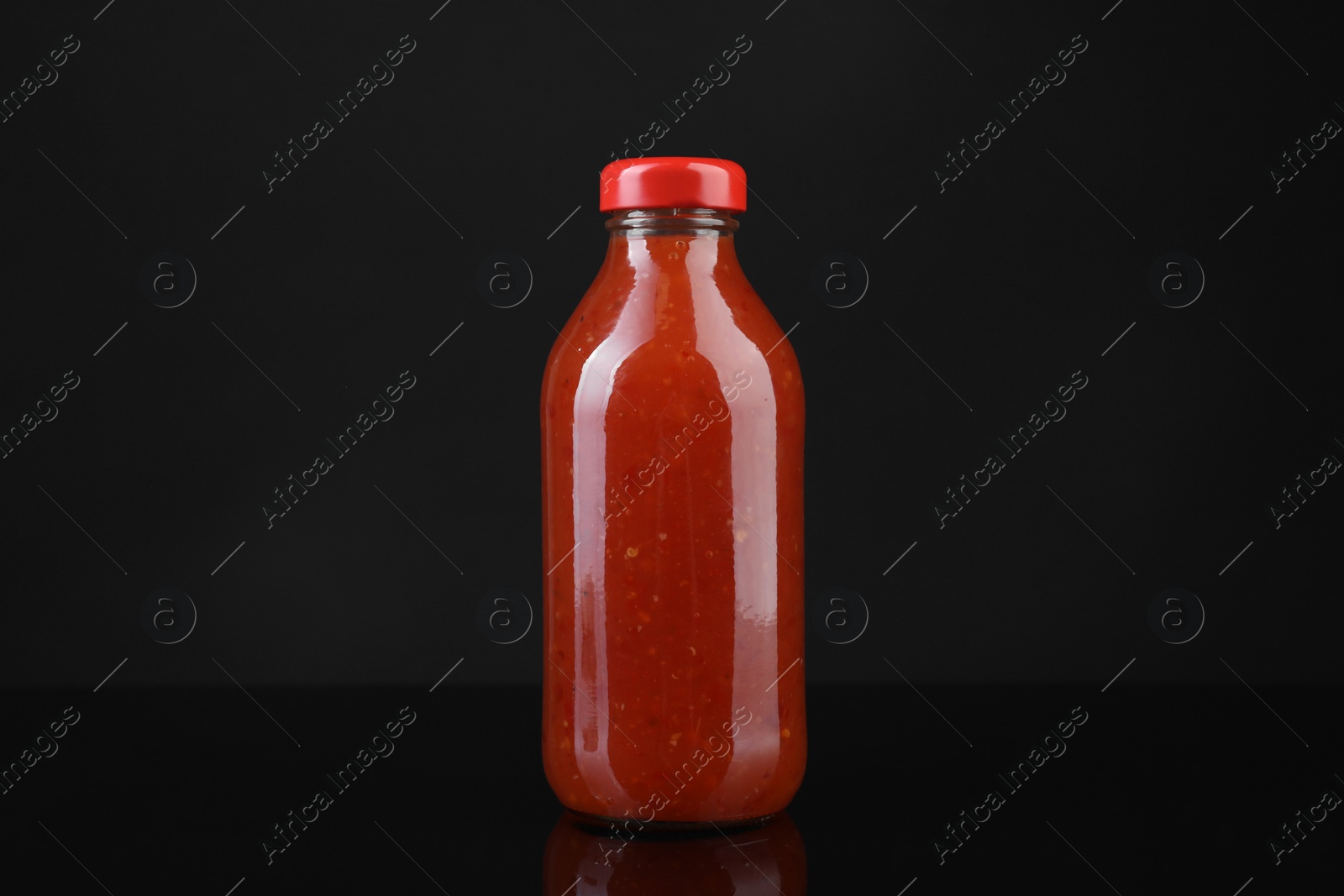 Photo of Spicy chili sauce in bottle on against dark background