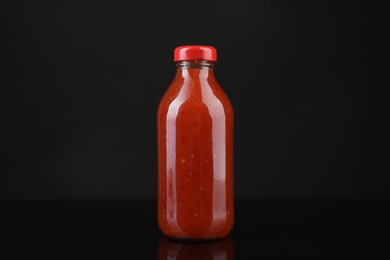 Photo of Spicy chili sauce in bottle on against dark background