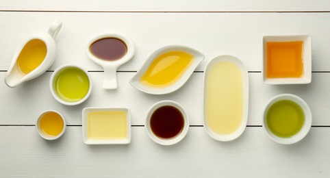 Photo of Vegetable fats. Different cooking oils on white wooden table, flat lay