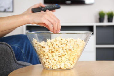 Young woman watching TV while eating popcorn at home, closeup
