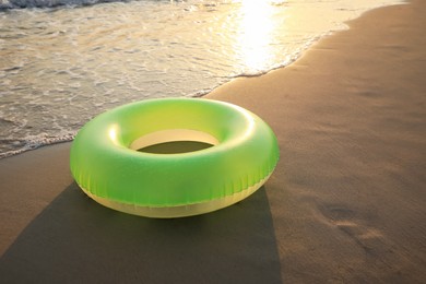 Light green inflatable ring on sunlit sandy beach near sea