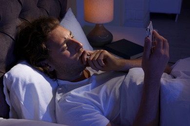 Handsome young man using smartphone in dark room at night. Bedtime