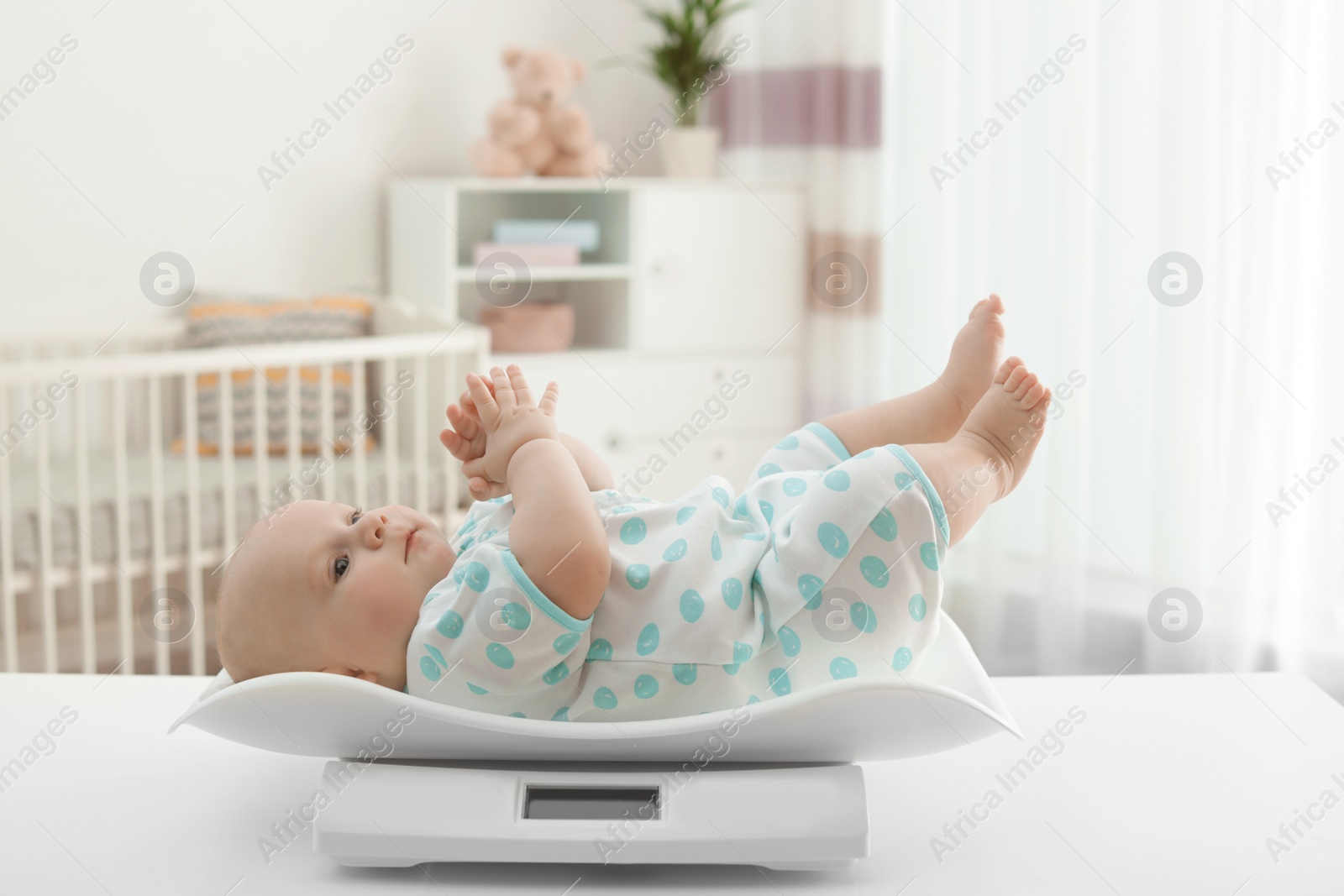 Photo of Cute little baby lying on scales in light room