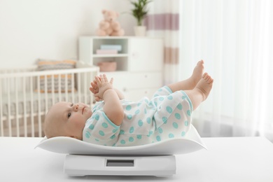 Photo of Cute little baby lying on scales in light room