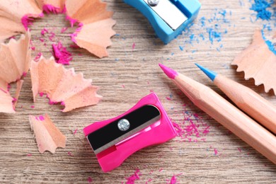 Sharpeners, colorful pencils and shavings on wooden table, flat lay