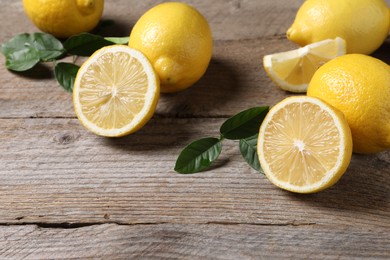 Photo of Fresh lemons and green leaves on wooden table, closeup