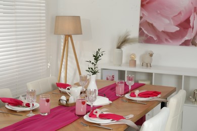 Color accent table setting. Glasses, plates, pink napkins and vase with green branch in dining room