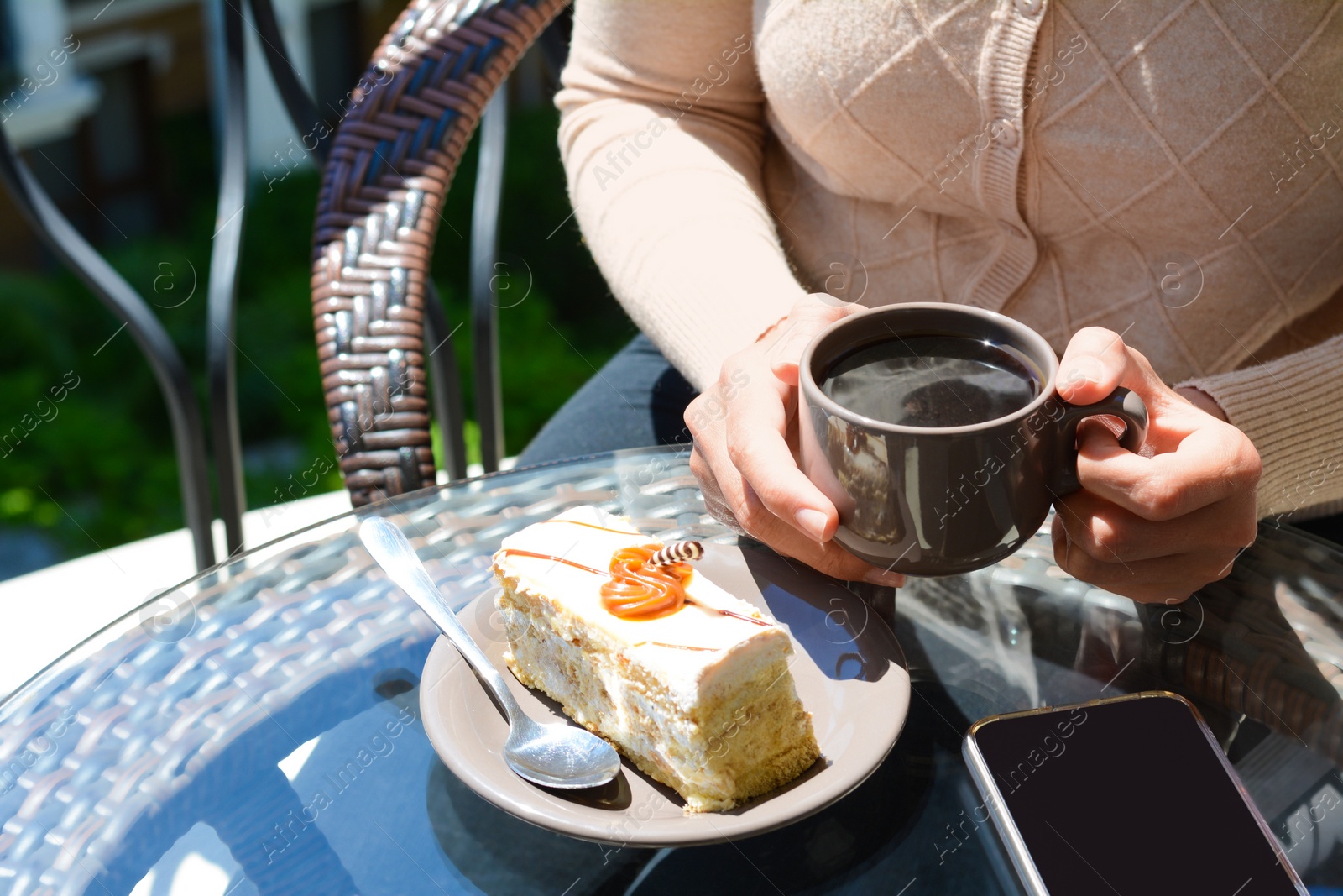 Photo of Woman with cup of coffee and tasty dessert at glass table outdoors, closeup