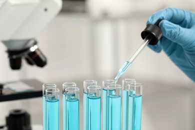 Photo of Scientist dripping liquid from pipette into test tube in laboratory, closeup