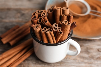 Photo of Mug with aromatic cinnamon sticks on wooden background