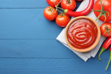 Photo of Bowl of tasty ketchup, tomatoes and peppers on blue wooden table, flat lay. Space for text