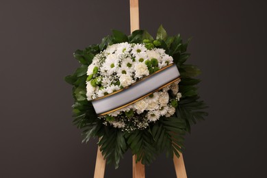 Funeral wreath of flowers with ribbon on wooden stand against grey background